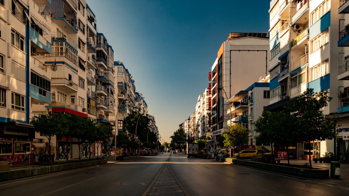 A deserted city street flanked by tall residential buildings in warm sunlight.